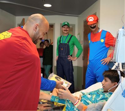 A man dressed as Superman visits with a pediatric patient.