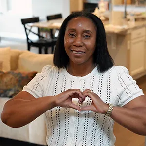 Denver Health breast cancer patient Catherine Thompson stands in her home making a heart with her hands.