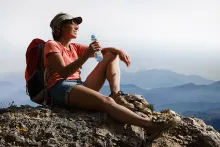 a female hiker beats the heat and sits on a mountain top, holding a bottle of water