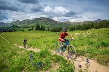Two kids ride mountain bikes up a hill with mountains in the background