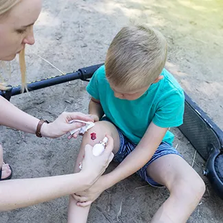 A mother attends to her young son after he cut his knee from falling off his scooter.